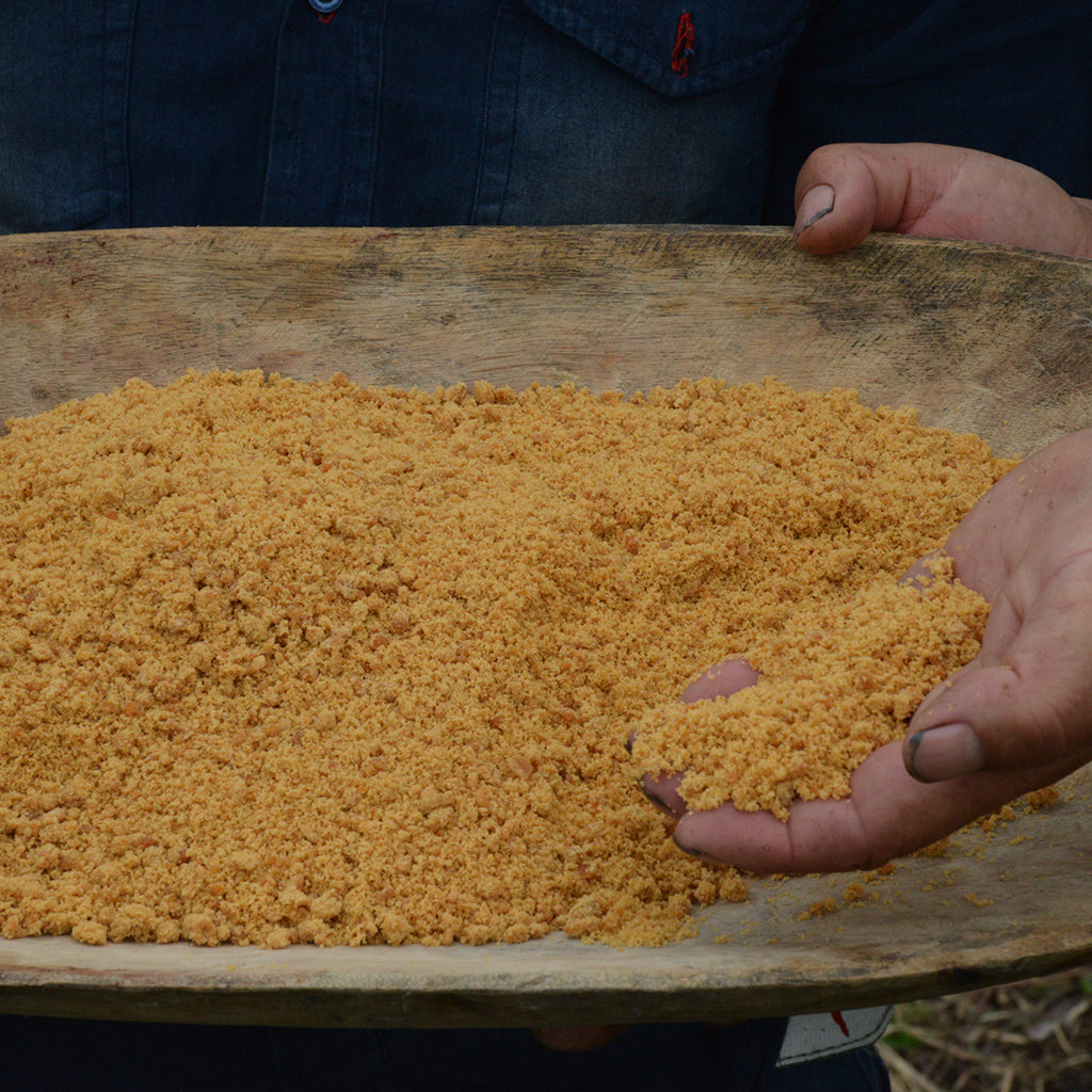 Closeup hand lifts cane sugar from wooden dish